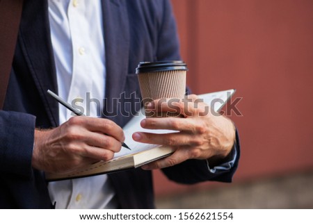 Notepad And A Cup Of Coffee In Hand Closeup Shot. A Man Makes Notes In His Notebook. Business Concept Photo