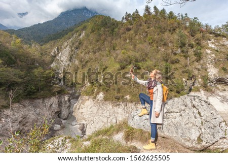 Young woman takes a picture of a mountain landscape in the Dolomiti Bellunesi National Park, sitting on a boulder, Italy. Concept: relaxation in nature, landscape photography, travel