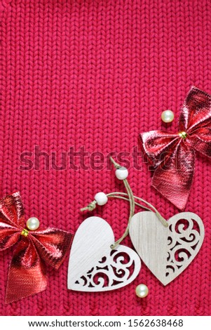 Greeting romantic card for Valentine's day. Festive background with a knitted texture, bows and wooden hearts with pattern. The symbol and sign of love lies on a red woolen fabric.
