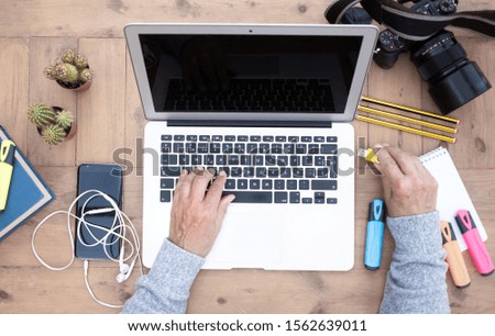 Aerial view of senior woman's hands working on laptop outdoor on a wooden table. Alternative outdoor office. Book, devices and camera close to her