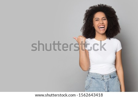 Excited African American girl laughing, pointing aside to copy space, presenting product, funny news, satisfied customer recommending service, shopping discount offer isolated on grey background