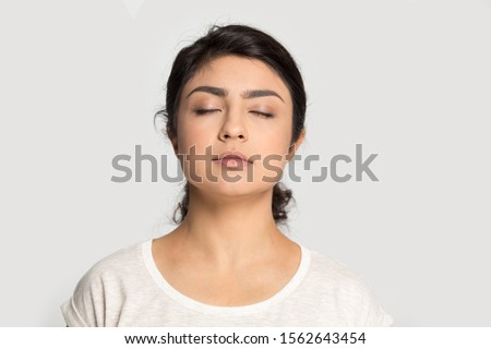 Calm Indian girl with closed eyes breathing deep, meditating, dreaming about future close up isolated on grey studio background, mindful young woman enjoying fresh air, taking break, pause