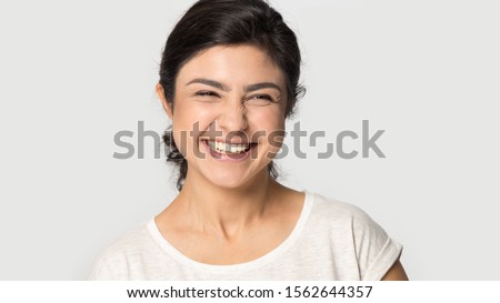 Head shot portrait excited Indian pretty girl laughing out loud at funny joke close up, happy beautiful young woman with beaming healthy smile standing isolated on grey studio background