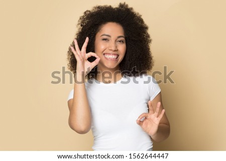 Head shot portrait close up smiling African American girl speaking sign language, standing isolated on brown background, deaf speechless young female communicating, looking at camera Royalty-Free Stock Photo #1562644447