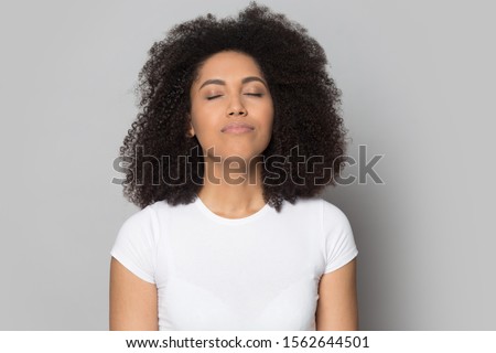 Head shot close up relaxed African American girl with closed eyes breathing deep, meditating, dreaming about future, isolated on grey studio background, mindful female enjoying break, pause