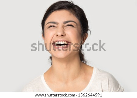 Head shot portrait close up excited Indian young woman laughing out loud at funny joke on grey background, pretty happy girl having fun, rejoicing success, satisfied by good news, feeling positive