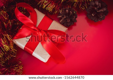 New Year's gift with a red ribbon in craft brown paper. Christmas composition of cones, tinsel and gifts on a red background.