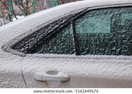 The car, covered with thick layer of snow. Negative consequence of heavy snowfalls. Side hundred cars with different patterns.