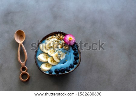 Blue spirulina smoothie bowl topped with fruit, nuts and flower on concrete background