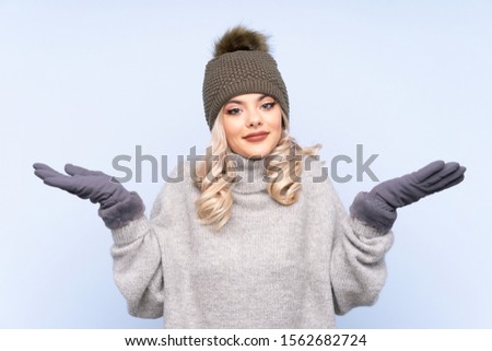 Young teenager girl with winter hat over isolated blue background having doubts with confuse face expression