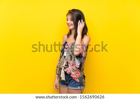 Caucasian girl in colorful dress over isolated yellow background listening to music with headphones