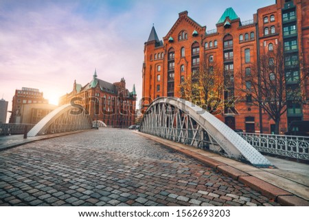 Arch bridge over alster canals with cobbled road in historical Speicherstadt of Hamburg, Germany, Europe. Scenic view of red brick building lit by golden sunset light Royalty-Free Stock Photo #1562693203
