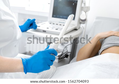 A gynecologist sets up an ultrasound machine to diagnose a patient who is lying on a couch. A transvaginal ultrasound scanner of the internal organs of the pelvis. Female health concept. Royalty-Free Stock Photo #1562704093