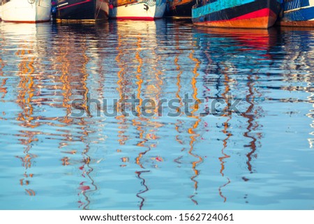 Row of vintage ship hulls at harbor, reflecting masts at blurred water surface foreground (copy space)