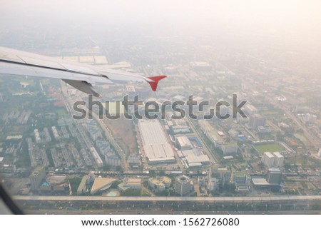 Wing of airplane before landing with cityscape in background.