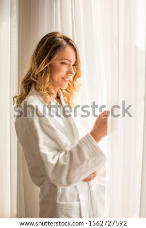 Attractive young woman looking through window in hotel room