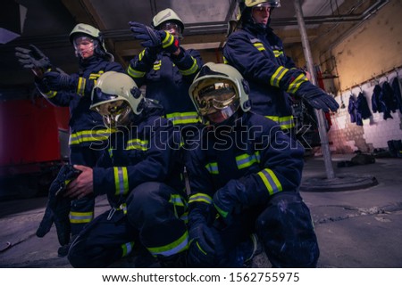 Portrait of group firefighters in front of firetruck inside the fire station wearing full protective gear with helmets on