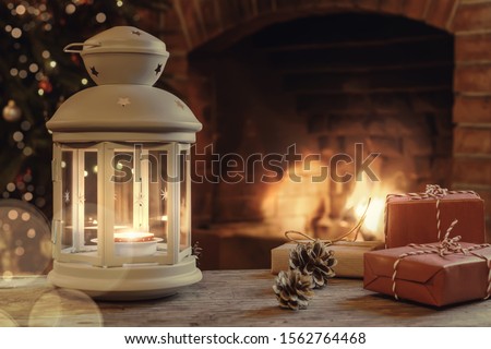 Lantern with a burning candle, gifts on a wooden table in a room with a Christmas tree and a fireplace on Christmas Eve