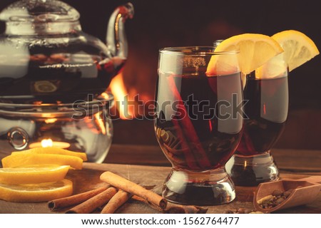 Two glasses of mulled wine and teapot on a wooden table in front of a burning fireplace