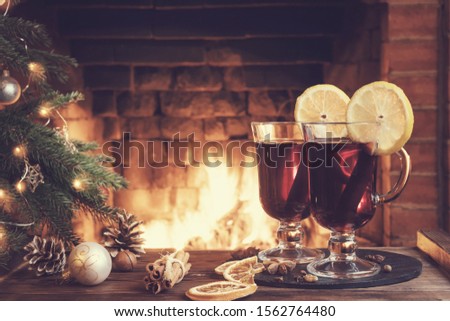 Christmas composition - two glasses with mulled wine on a wooden table near a Christmas tree opposite a burning fireplace