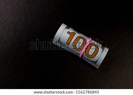 Black background. close-up. 100 dollars you rolled up and tied an elastic band.
