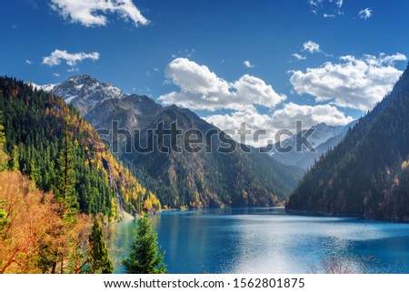 Fantastic view of the Long Lake among colorful fall woods and snow-capped mountains in Jiuzhaigou nature reserve (Jiuzhai Valley National Park), China. Beautiful snowy peaks are visible in background. Royalty-Free Stock Photo #1562801875