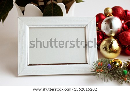 White color,wooden empty picture frame stand in front of christmas ball and poinsettia flower.