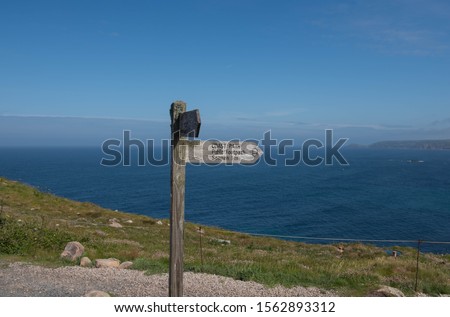 Sign Post to Sennan Cove and Way Marker for a Public Footpath and South West Coast Path on a Cliff Top with a Bright Blue Sea and Sky Background