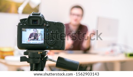 Camera on a tripod filming a blogger at home sitting on his workspace