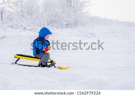 little boy rides a snow scooter in winter