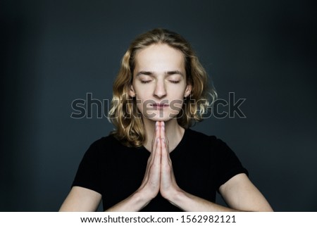 Young attractive man  is meditating cupped in a meditation or prayer gesture  with a pacified face   on a gray background