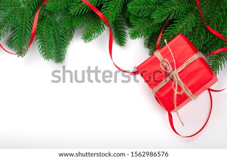 Holiday frame with Christmas tree branches and decorations with small red gift box and red stripe on white wooden background.  Christmas background template for greetin0g cards and social media.