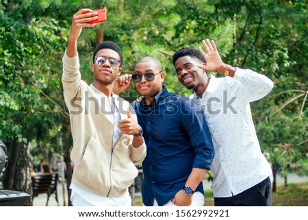 a group of three fashionable cool African American guys students communicating on the street looking at smartphone take pictures selfie on phone in street.