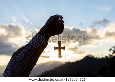 Silhouette human praying to the GOD while holding a crucifix symbol with bright sunbeam on the sky