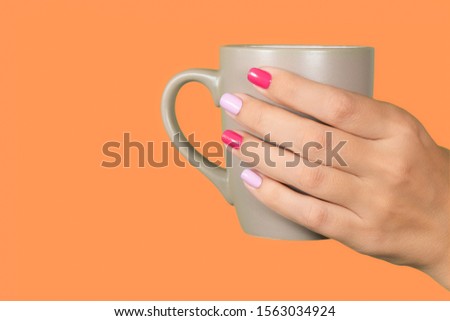Closeup view of beautiful manicured female hand holding mug isolated on bright orange background. Horizontal color photography.