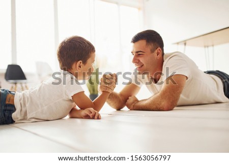 Father and son lying down on the ground and playing arm wrestling.