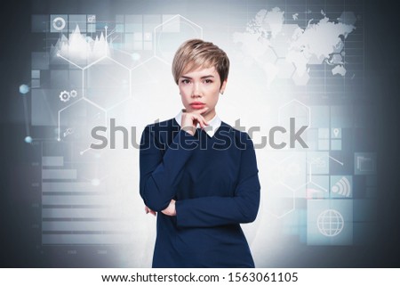 Portrait of serious young businesswoman in blue dress standing near gray wall with infographics drawn on it. Concept of big data. Double exposure. Elements of this image furnished by NASA