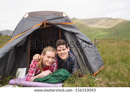 Happy couple lying in their tent and looking at camera in the countryside