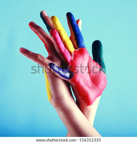 Child's hands painted with multicolored finger paints on blue background as a help concept