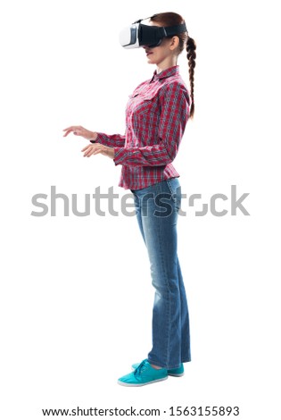 Young woman wearing VR goggles and working with virtual interface. Woman standing and touching air during using VR-headset glasses of virtual reality. Studio photo by girl against gray background