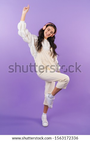 Photo of positive optimistic cheery brunette woman posing isolated over purple wall background listening music with headphones dancing.