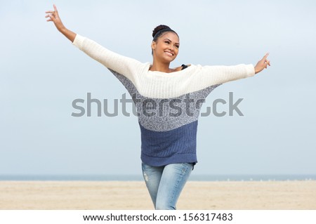 Closeup portrait of a beautiful young woman with cheerful expression and arms outstretched walking at the beach