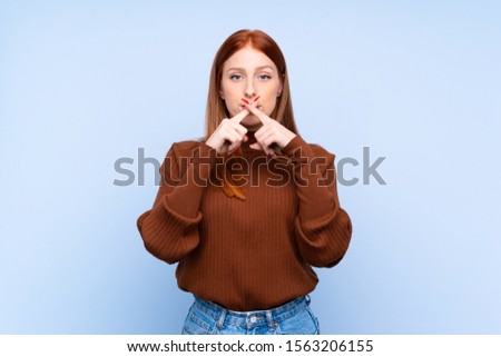 Young redhead woman over isolated blue background showing a sign of silence gesture