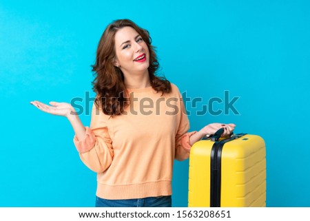 Traveler woman with suitcase over isolated blue background holding copyspace imaginary on the palm