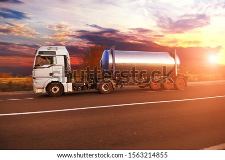 Big metal fuel tanker truck shipping fuel on the countryside road with forest against night sky with sunset