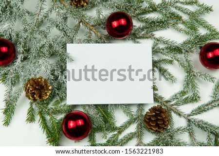 White card on the background of fir branches with cones and Christmas toys on a white wooden background. Mock up, copy space