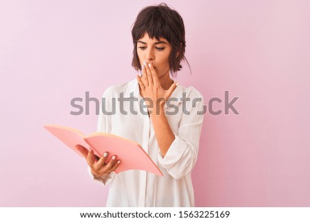 Young beautiful teacher woman reading book standing over isolated pink background cover mouth with hand shocked with shame for mistake, expression of fear, scared in silence, secret concept