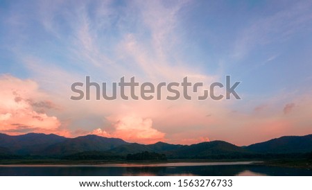 Picture of a lake surrounded by mountains With a backdrop of orange-pink skies.