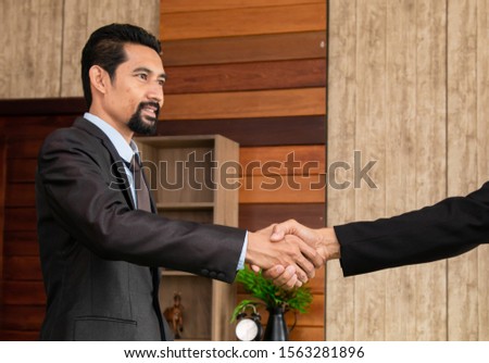 Smart Asian business man in formal suit with beard shaking hands finishing sign contract business deal with partner at workplace office, mature business executive shake hands for agreement discussion