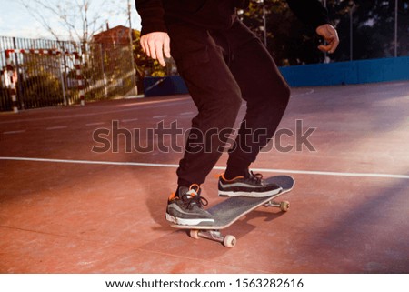 The young individual legs of the male skateboarder just ride a skateboard preparing to jump in an urban area in a skatepark with long black pants and sneakers